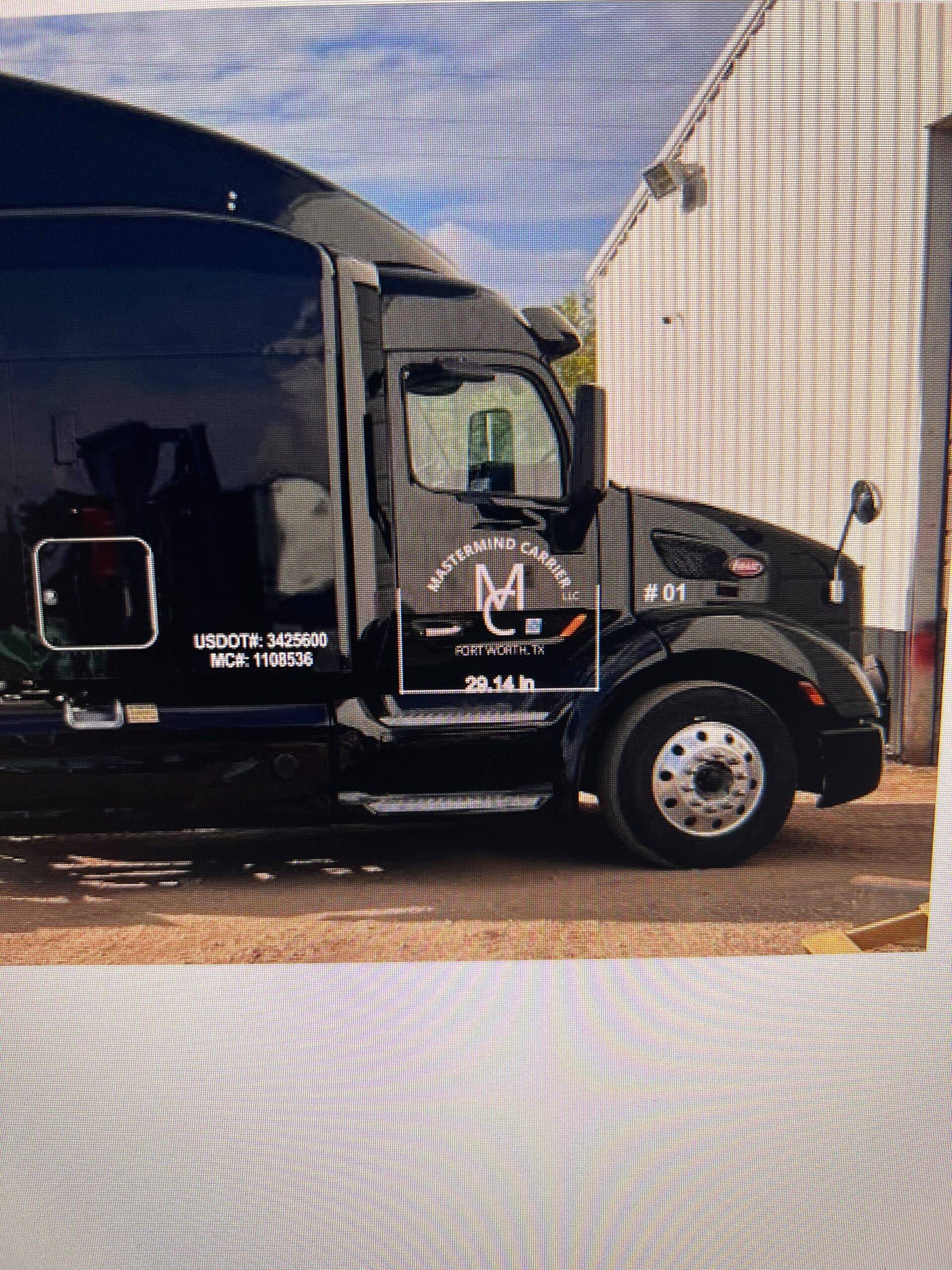 A polished black Peterbilt truck parked at the Mastermind Carrier Trucking LLC headquarters in Fort Worth, Texas. The company name and logo are professionally printed on the side doors of the pristine truck, exemplifying the modern, well-maintained fleet utilized to provide reliable transportation solutions.